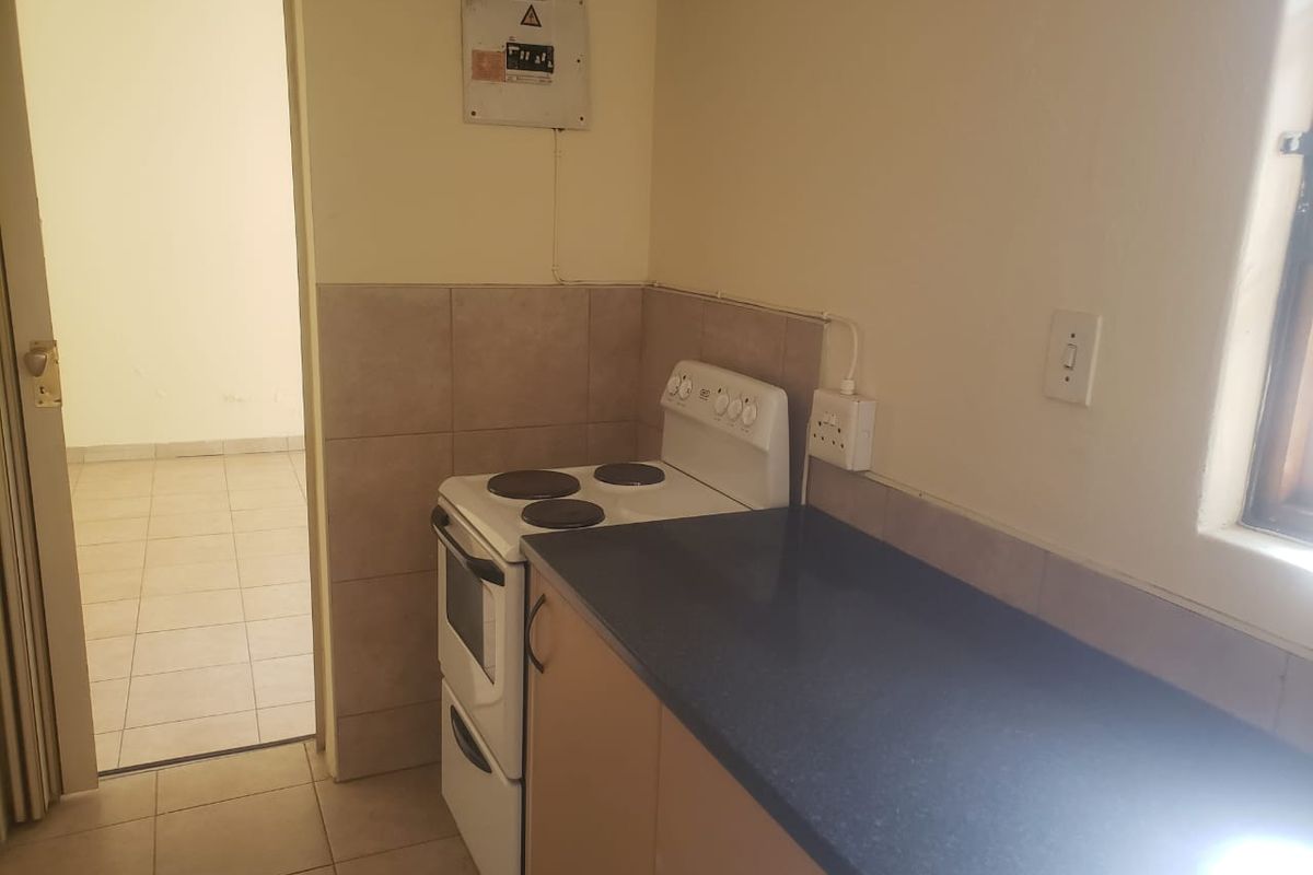 A compact kitchen area featuring a freestanding stove, laminate countertop, and tiled splashback, with an adjacent doorway leading to an empty room.