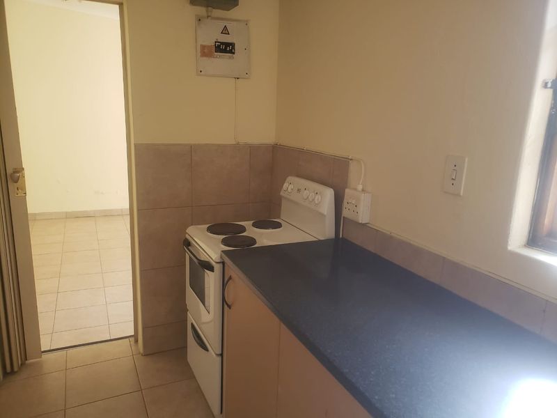 A compact kitchen area featuring a freestanding stove, laminate countertop, and tiled splashback, with an adjacent doorway leading to an empty room.