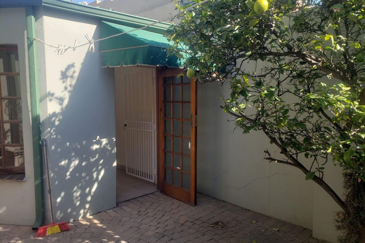 A rear exterior view featuring brick paving, a timber-framed glass door with a security gate, and a green fabric awning.