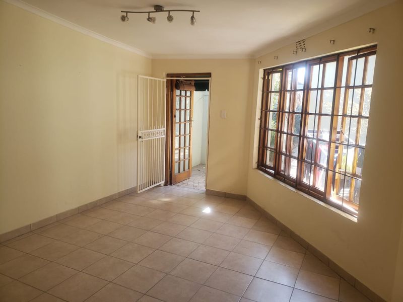 An empty living room featuring tiled flooring, wooden window frames, and a security gate, offering a blank canvas for personalization.