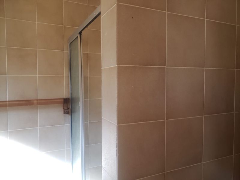 A close-up view of a bathroom shower area featuring neutral wall tiles and a framed shower enclosure.