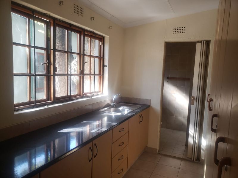 A functional scullery or utility area featuring built-in cabinetry, a stone countertop with a stainless steel sink, and tiled flooring.