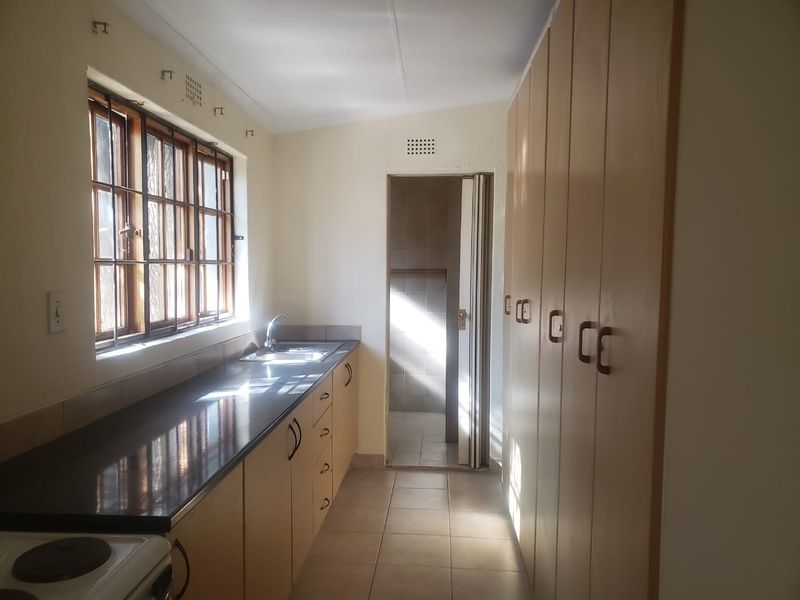 A functional scullery or utility area featuring built-in cabinetry, ample storage cupboards, a stainless steel sink, and tiled flooring.