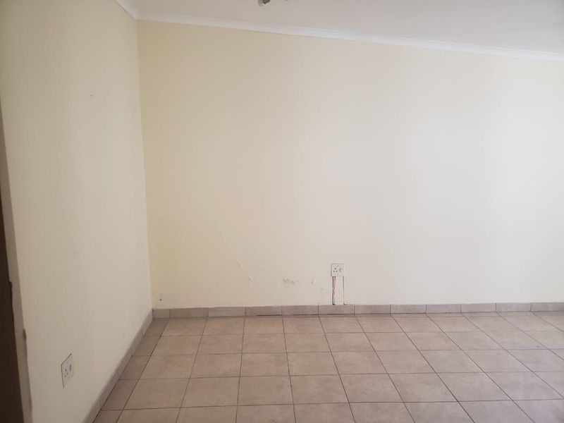 An empty living area featuring neutral ceramic floor tiles and coved ceiling cornices, requiring minor wall repairs and cosmetic updates.