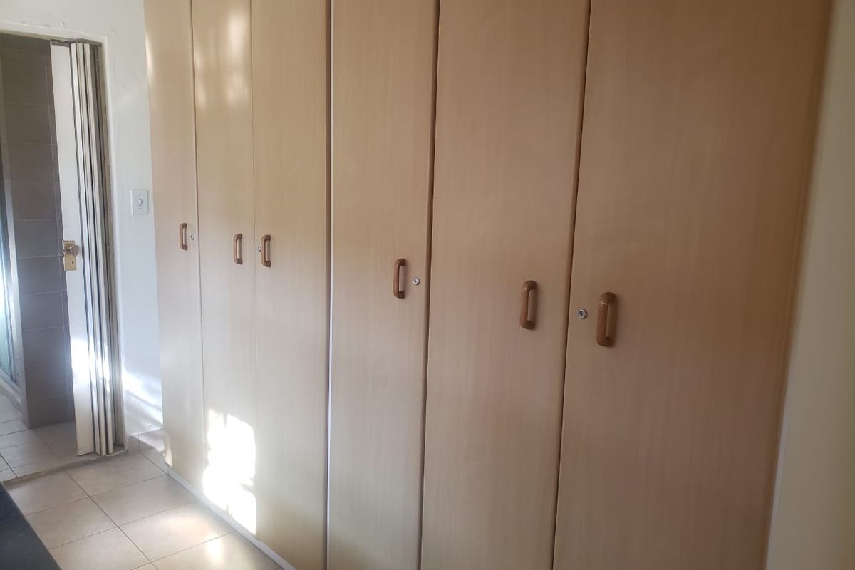 A bedroom featuring extensive built-in wooden cupboards and tiled flooring, with a folding door leading to an adjacent space.