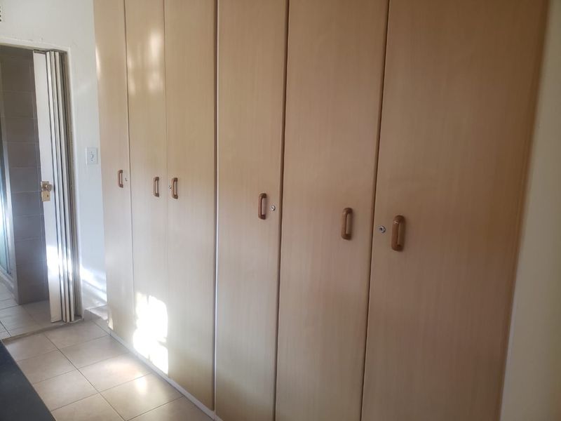 A bedroom featuring extensive built-in wooden cupboards and tiled flooring, with a folding door leading to an adjacent space.