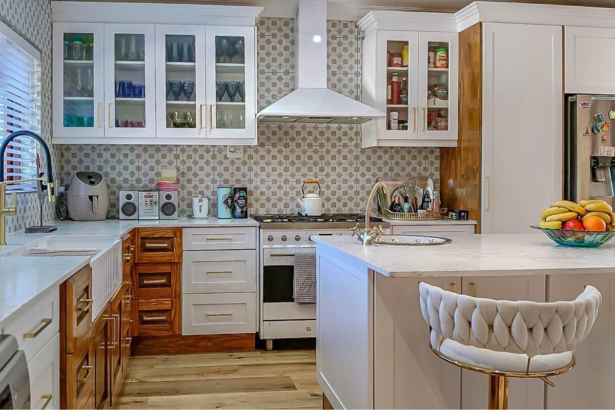 A well-appointed kitchen featuring a farmhouse sink, gas stove with extractor, central island, and a mix of white and natural wood cabinetry.