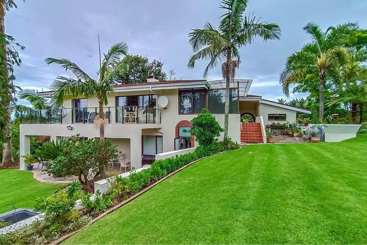 Rear view of a multi-level farm property featuring a spacious balcony, paved patio area, tiled staircase, and well-maintained landscaped garden.