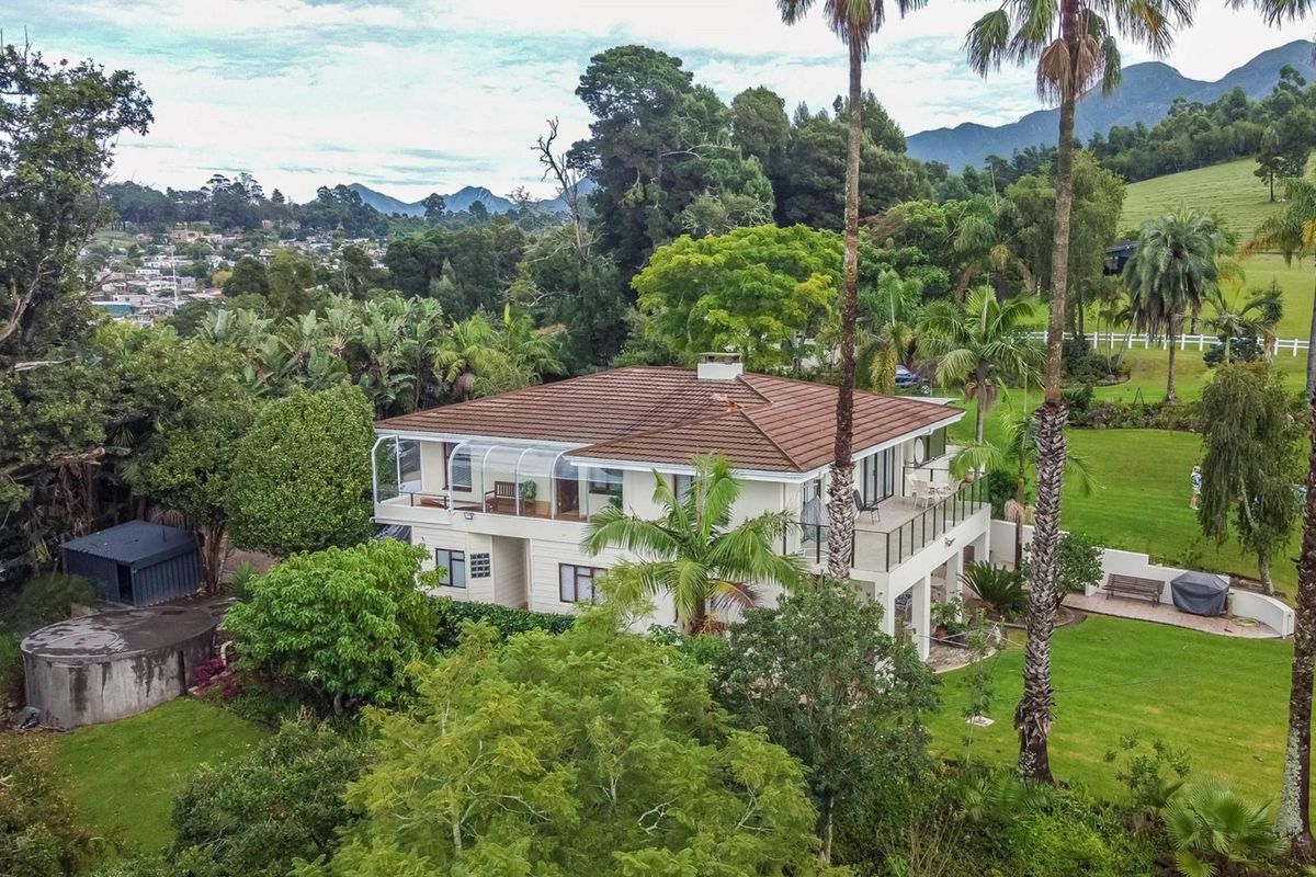 Aerial view of a multi-level farm residence featuring a tiled roof, expansive balconies, and a well-maintained garden set against a scenic landscape.