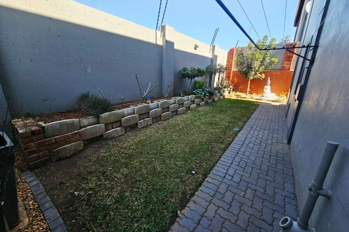 A private rear garden featuring a paved walkway, a raised brick retaining wall, and secure boundary walls with electric fencing.