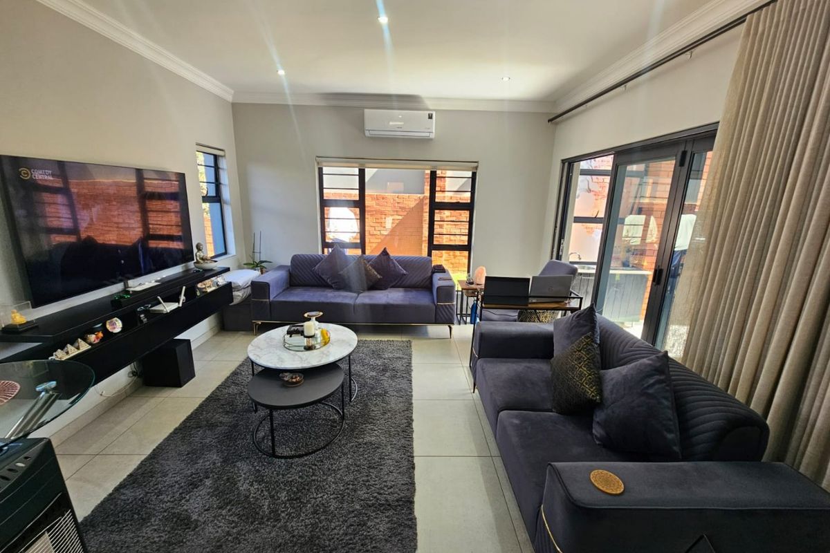 A well-maintained living room featuring tiled flooring, recessed downlighting, a wall-mounted air conditioning unit, and large sliding glass doors providing natural light.