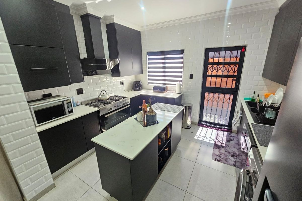 Modern kitchen featuring dark cabinetry, a central island with stone countertop, gas stove, extractor fan, and white subway tile backsplash.
