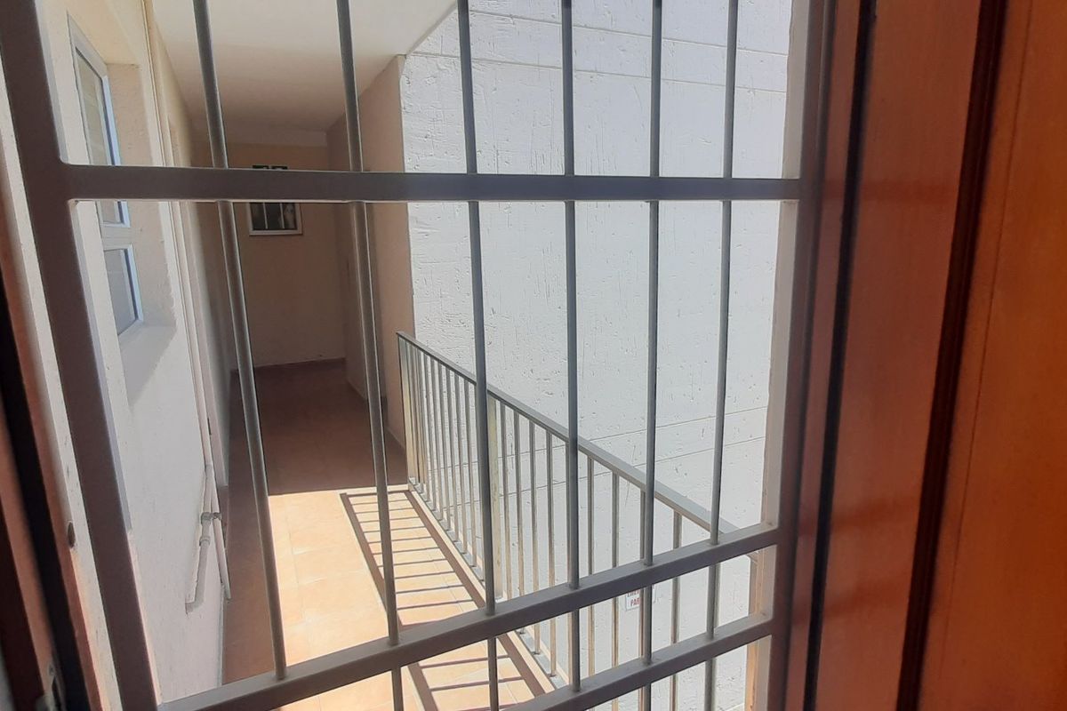 View of an apartment building exterior corridor featuring metal security bars and a balcony railing.