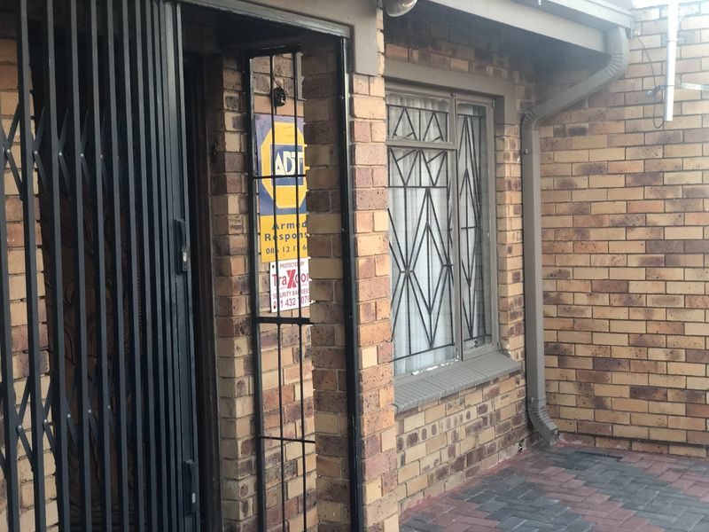 Front entrance of the townhouse featuring face brick exterior, security gates, and burglar bars for added safety.