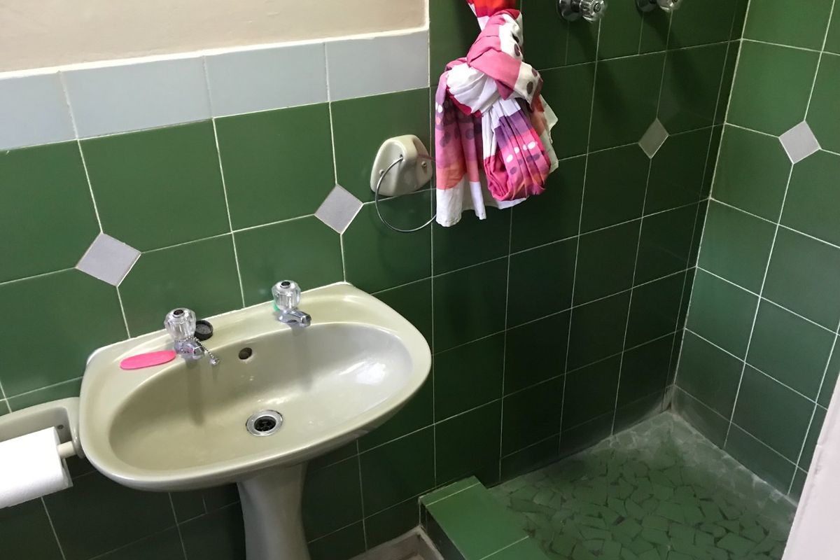 A dated bathroom featuring a pedestal basin and a tiled shower cubicle with green ceramic wall tiles and mosaic flooring.