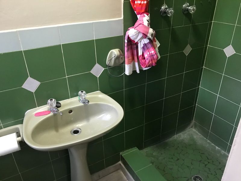 A dated bathroom featuring a pedestal basin and a tiled shower cubicle with green ceramic wall tiles and mosaic flooring.