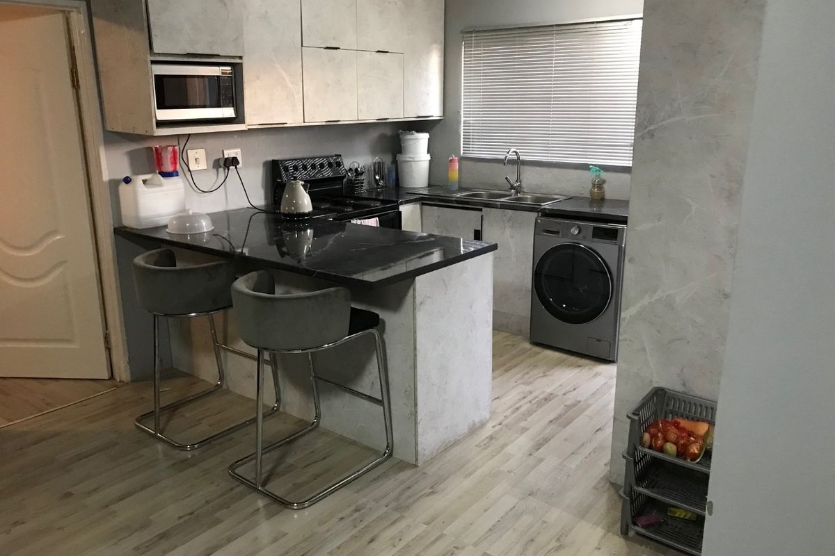 Functional kitchen featuring stone countertops, built-in cabinetry, a breakfast bar, and integrated appliances, finished with modern laminate flooring and neutral tones.