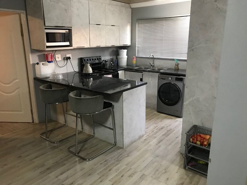 Functional kitchen featuring stone countertops, built-in cabinetry, a breakfast bar, and integrated appliances, finished with modern laminate flooring and neutral tones.