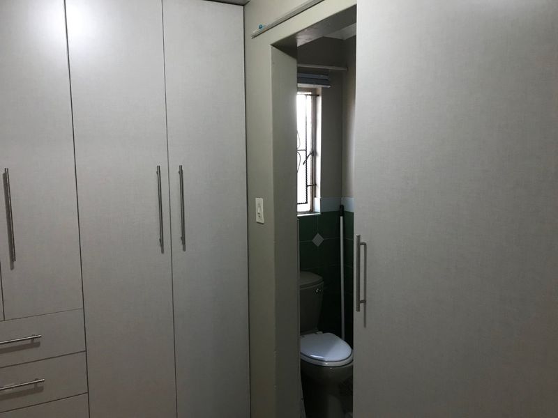 Bedroom featuring built-in cupboards with a direct view into an adjoining bathroom with a toilet.