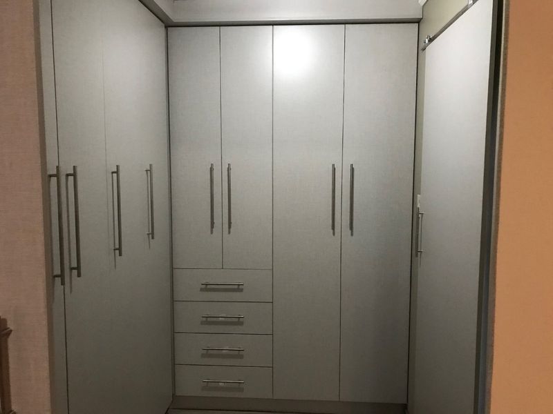 A clean and functional bedroom featuring extensive built-in cabinetry with integrated drawers and modern handles, providing ample storage space.