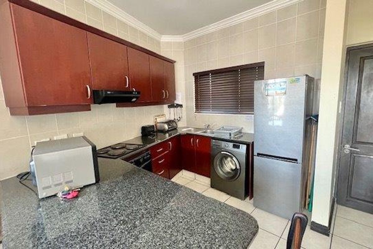 A functional kitchen featuring dark wood cabinetry, granite countertops, a tiled backsplash, and integrated appliances including an oven, hob, and extractor fan.