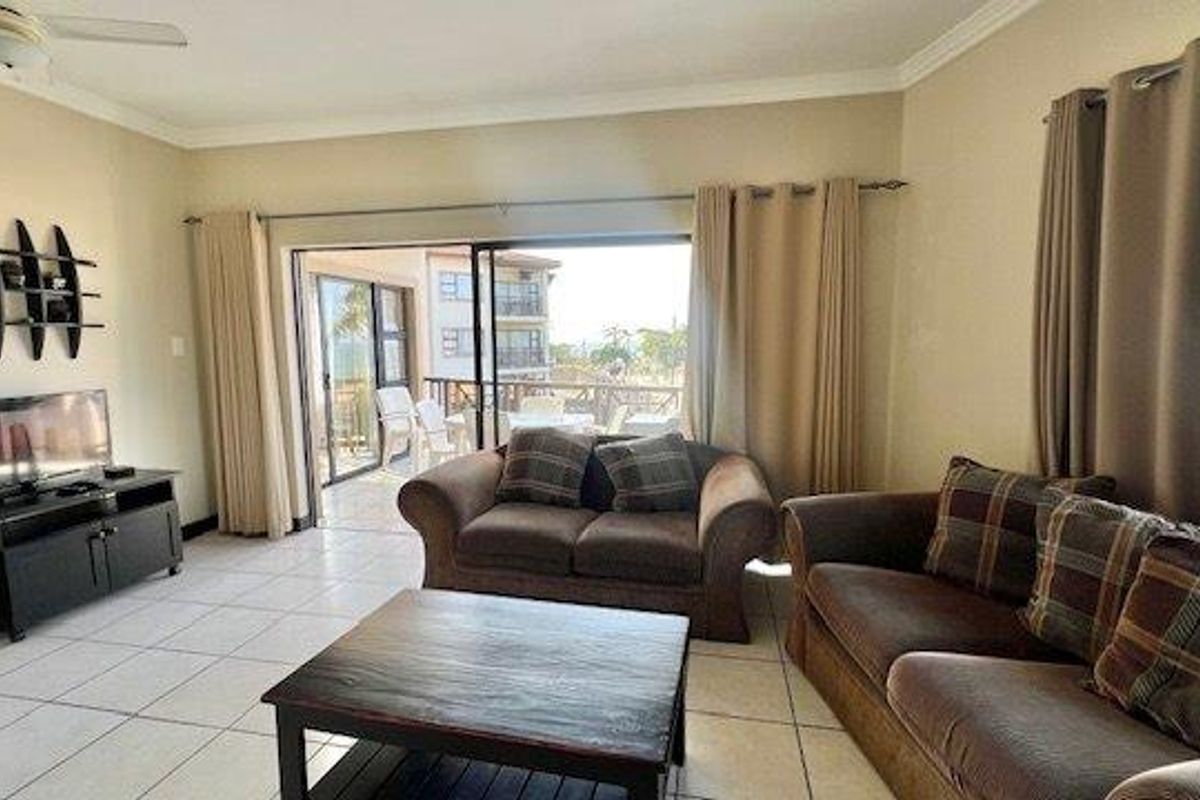 A living room featuring ceramic floor tiles, a ceiling fan, and large sliding glass doors that provide access to an outdoor balcony area.