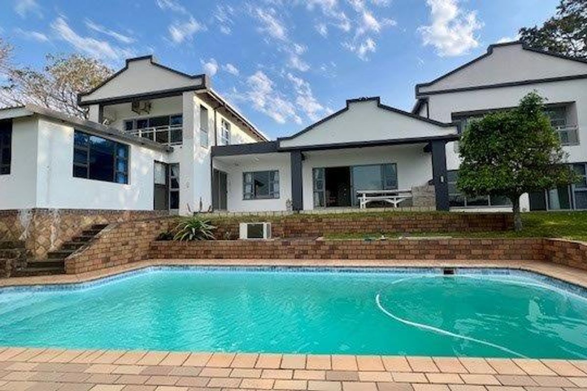 Rear view of the multi-level residence featuring a swimming pool, paved deck, tiered brick retaining walls, and a covered patio area.