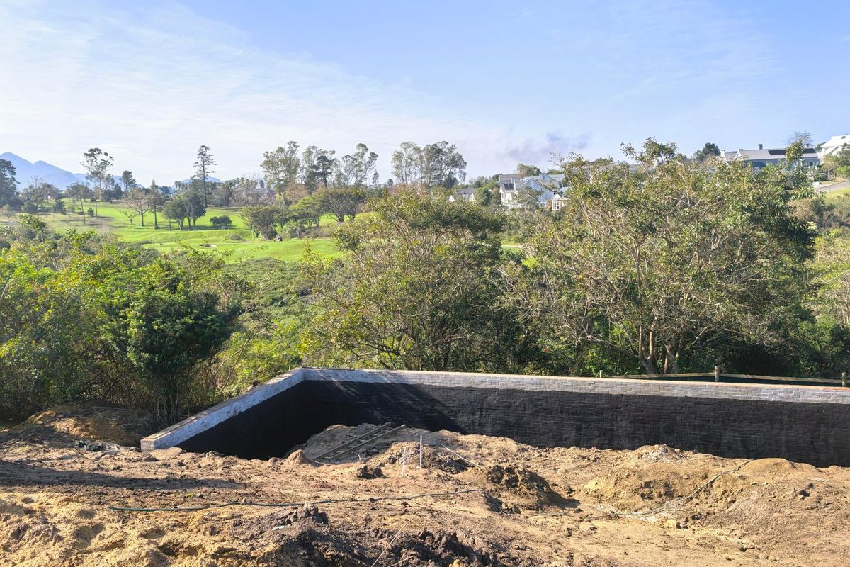A construction site showing a newly built retaining wall with waterproofing, overlooking a scenic golf course and surrounding landscape.