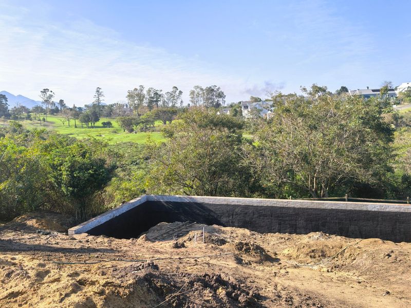 A construction site showing a newly built retaining wall with waterproofing, overlooking a scenic golf course and surrounding landscape.
