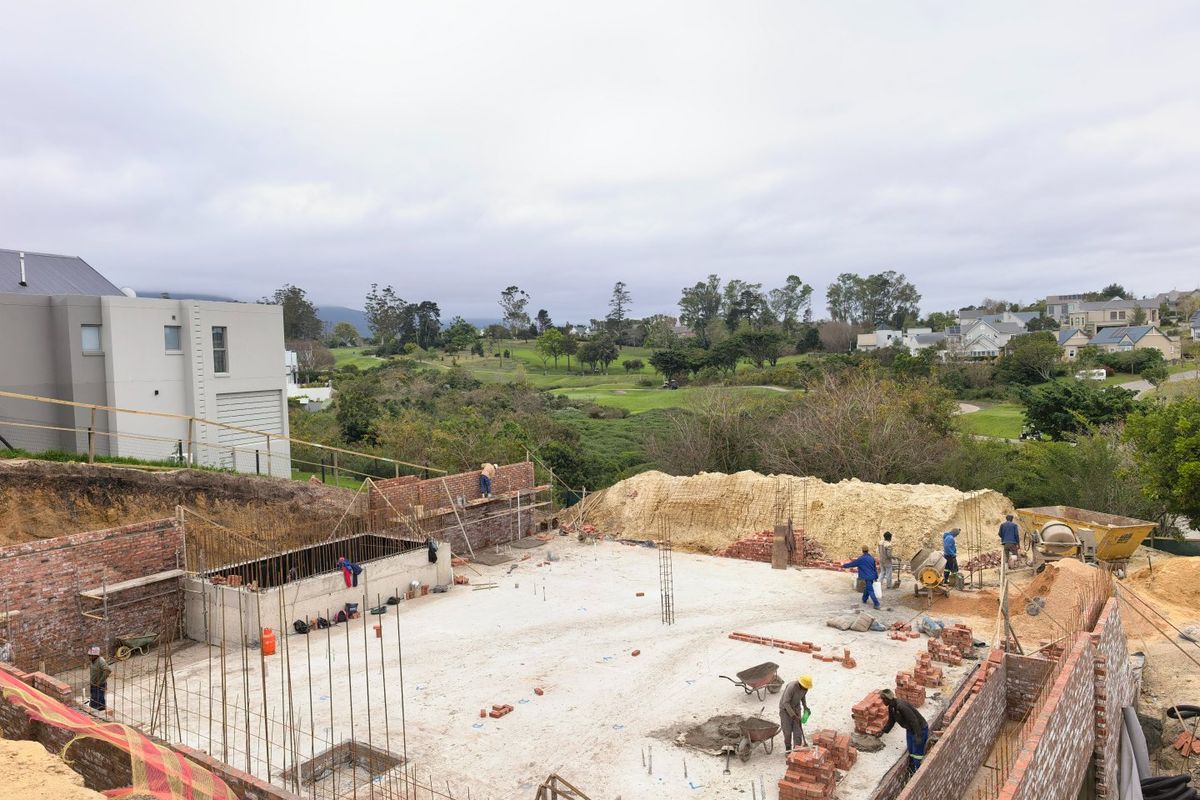 An elevated view of a residential property under construction, featuring concrete foundations and brick retaining walls in a scenic estate setting.