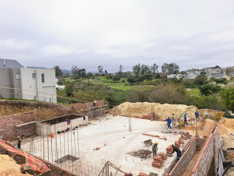An elevated view of a residential property under construction, featuring concrete foundations and brick retaining walls in a scenic estate setting.