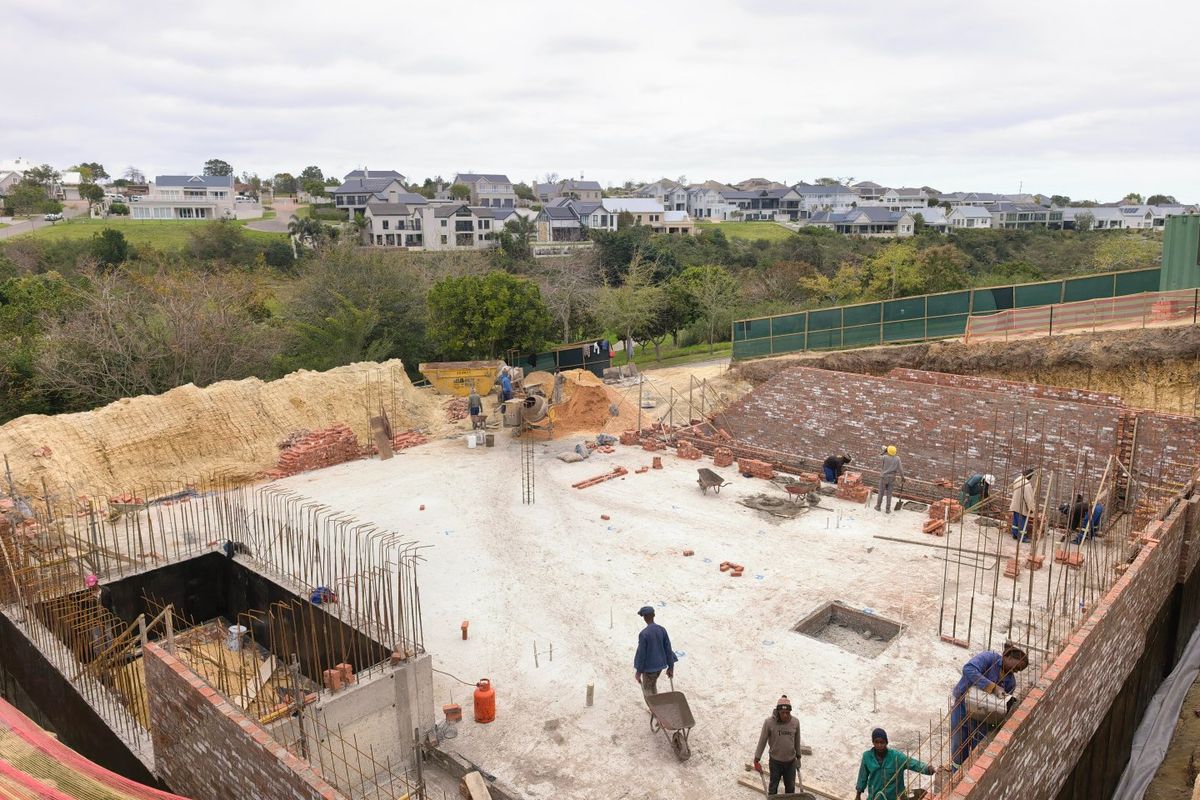 An elevated view of a residential construction site showing ongoing brickwork, concrete foundation, and structural reinforcement in a developing estate.