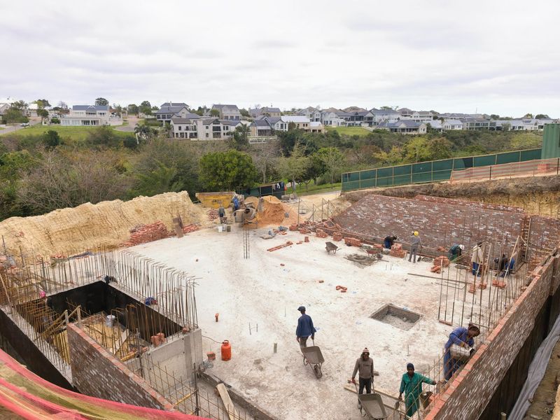 An elevated view of a residential construction site showing ongoing brickwork, concrete foundation, and structural reinforcement in a developing estate.