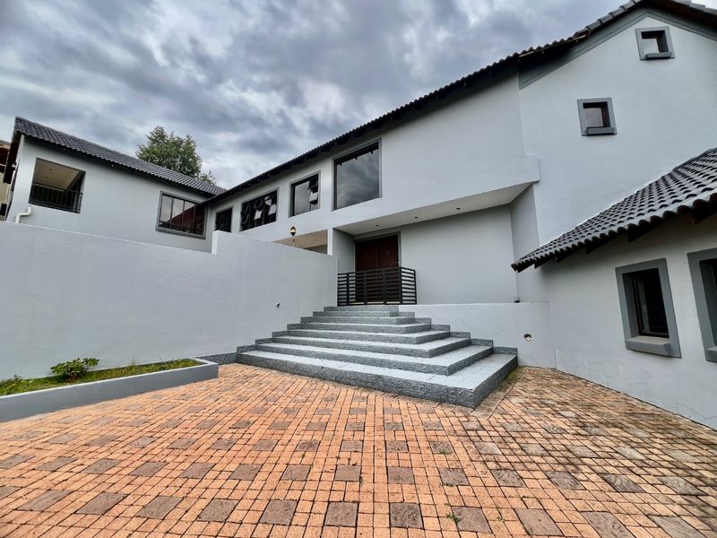 Front exterior view of a multi-level house featuring a paved driveway, concrete entrance staircase, and a double door entry.