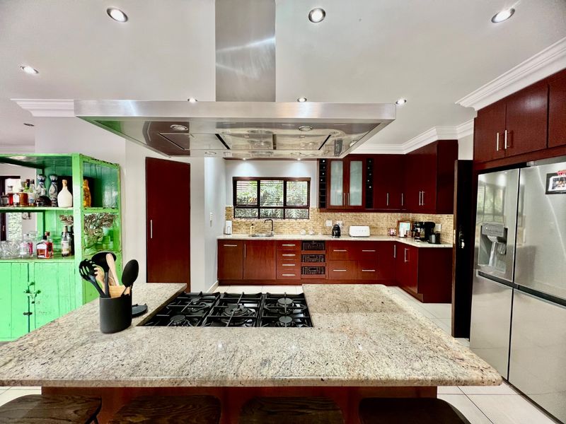 Spacious kitchen featuring dark wood cabinetry, granite countertops, a central island with a built-in gas hob, and a large stainless steel extractor hood.