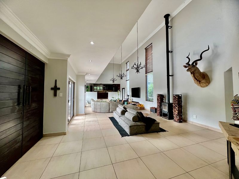 Spacious open-plan living area featuring high vaulted ceilings, tiled floors, a modern freestanding fireplace, and large windows providing ample natural light.