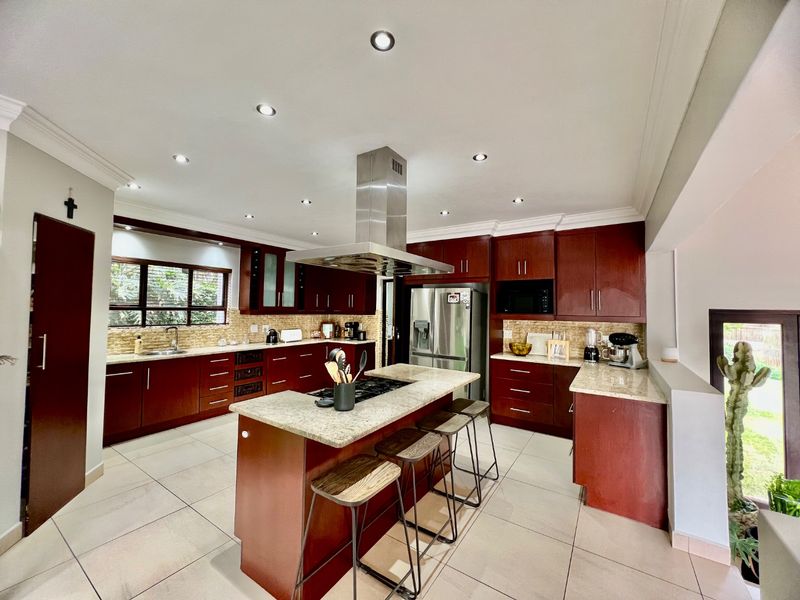 Spacious kitchen featuring dark wood cabinetry, stone countertops, a central island with a gas cooktop, and integrated stainless steel appliances.