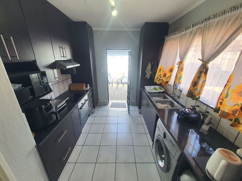 A functional galley-style kitchen featuring dark cabinetry, granite countertops, tiled flooring, and direct access to an outdoor patio area.