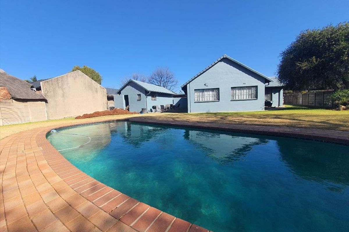 A spacious backyard featuring a large swimming pool with brick coping, surrounded by a lawn and the rear elevation of the house.