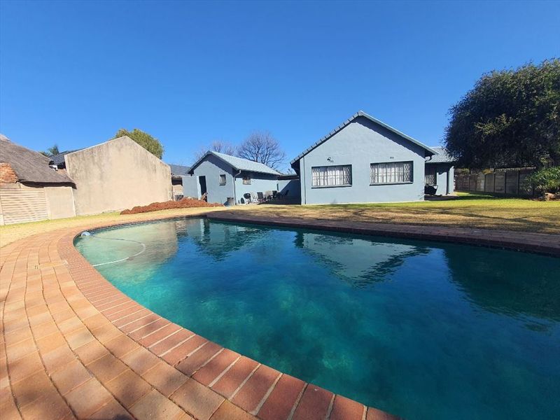 A spacious backyard featuring a large swimming pool with brick coping, surrounded by a lawn and the rear elevation of the house.