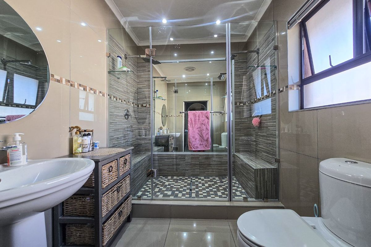 Modern bathroom featuring a spacious walk-in shower with a tiled bench, mosaic flooring, glass enclosure, pedestal basin, and neutral ceramic wall tiling.