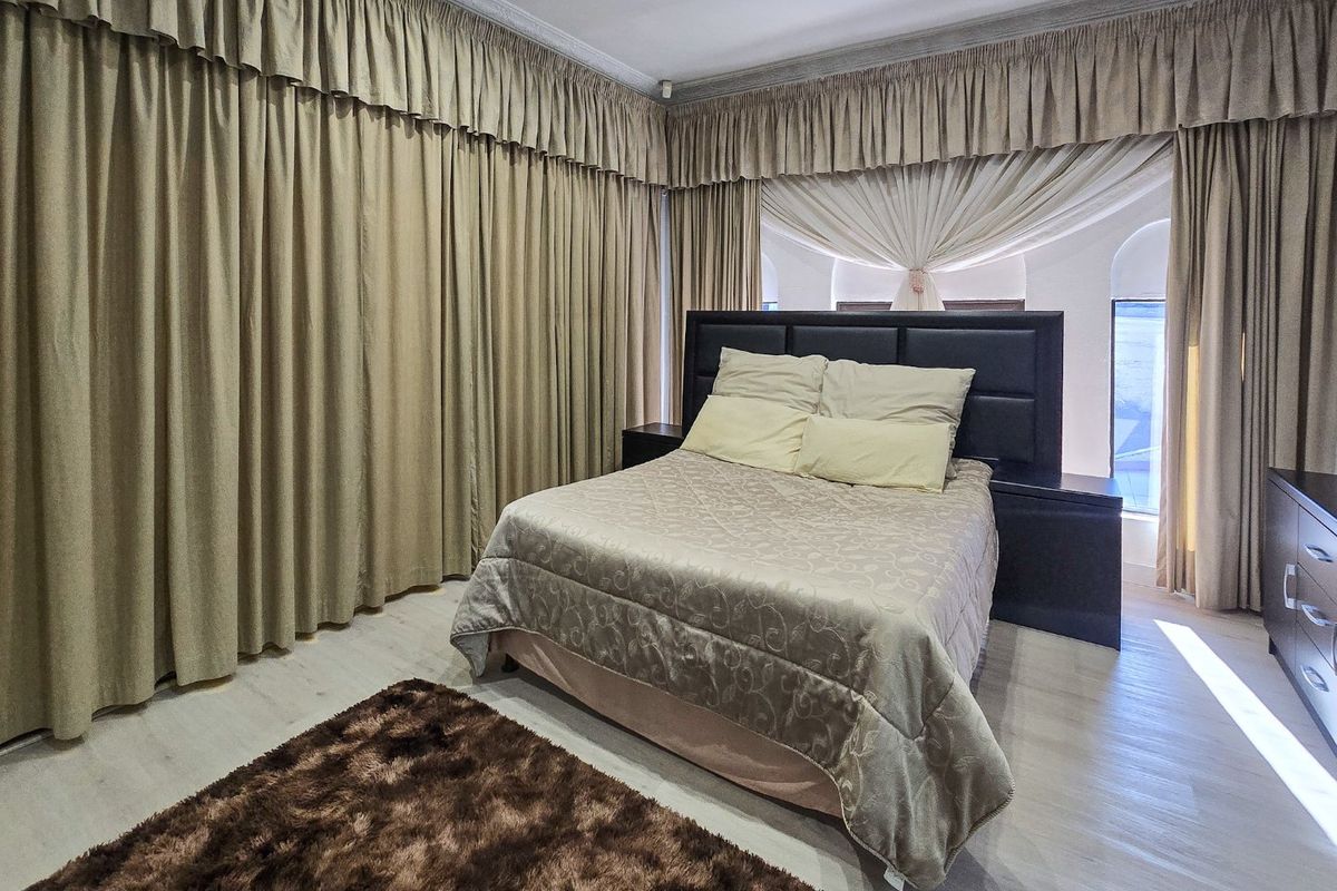 Spacious bedroom featuring laminate flooring, decorative coving, and extensive floor-to-ceiling window drapery.