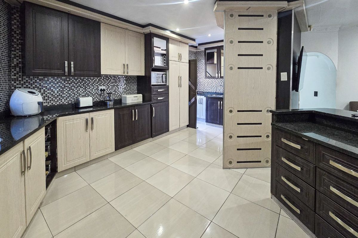 Modern kitchen featuring two-tone cabinetry, granite countertops, mosaic tile backsplash, and large format porcelain floor tiles with integrated lighting.