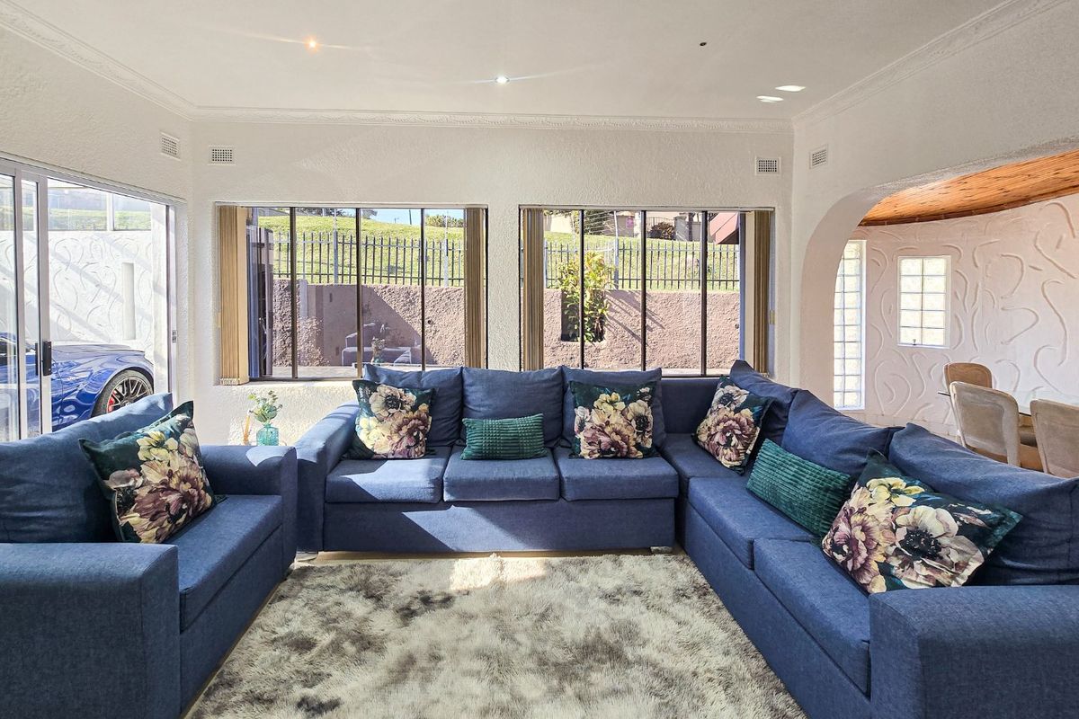 A bright living room featuring textured walls, decorative ceiling detailing, recessed lighting, and large windows providing natural light and garden views.