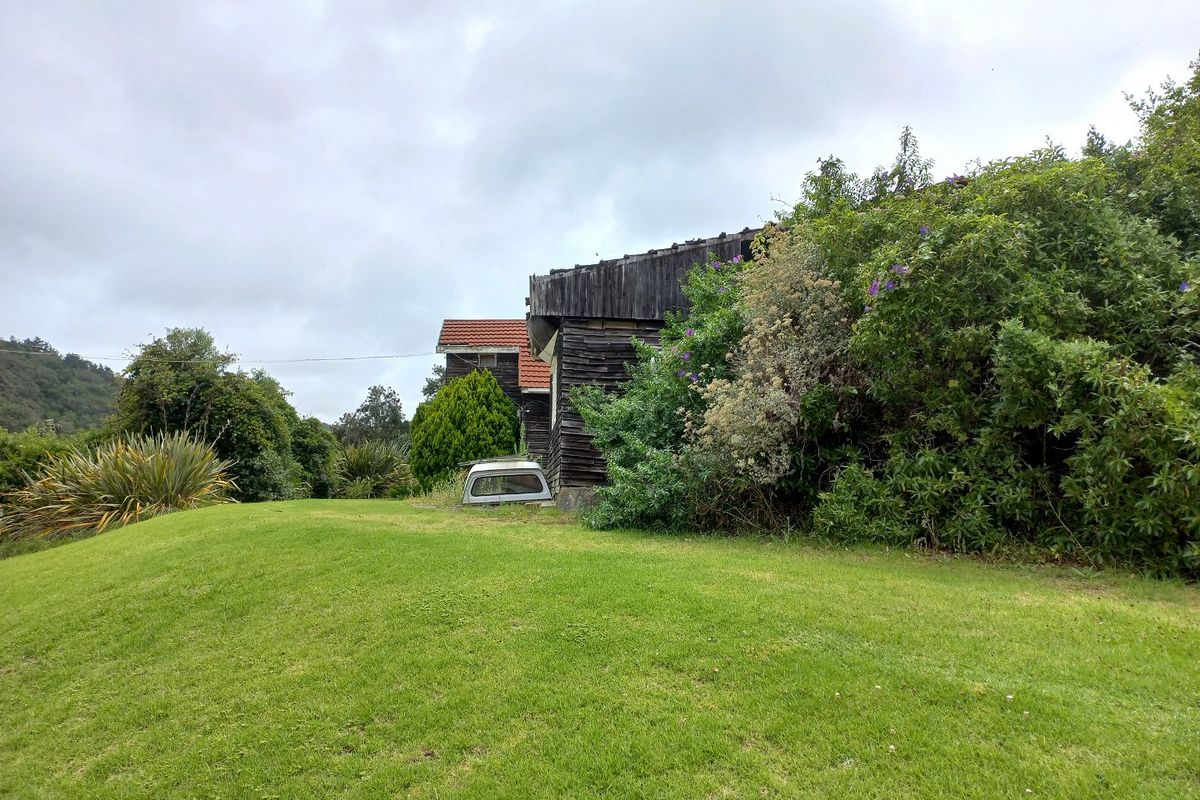 A view of the rear exterior of the property featuring weathered timber cladding and a tiled roof set against a large grassed area.