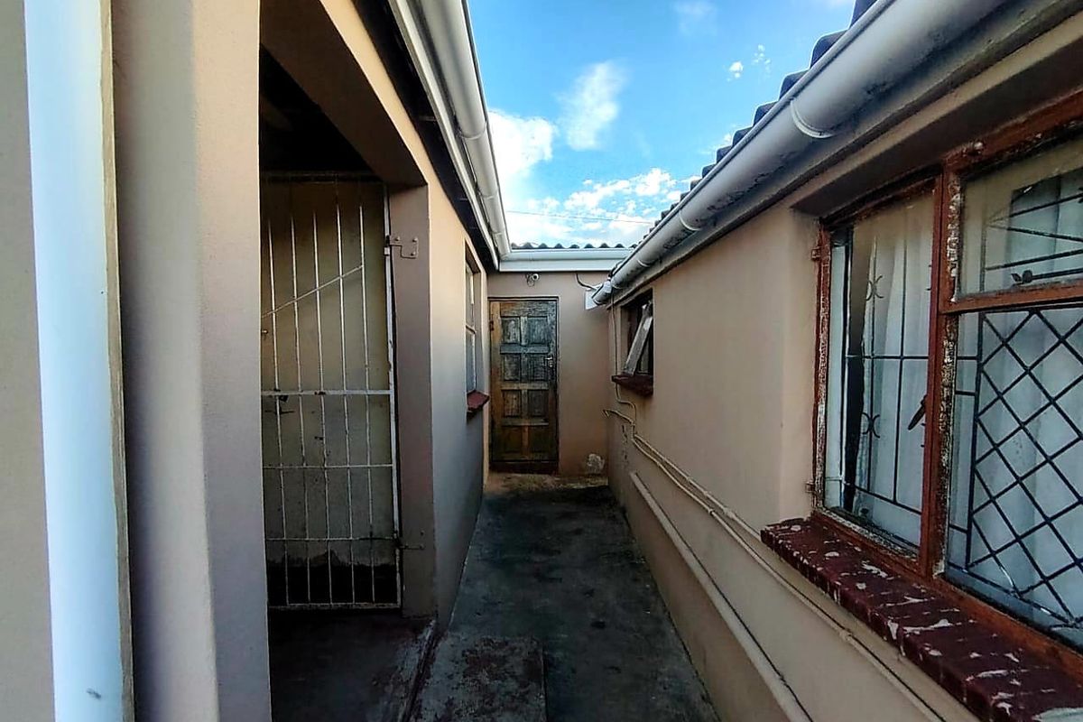 A narrow exterior side passage featuring security gates, timber door, and metal-framed windows with security bars.