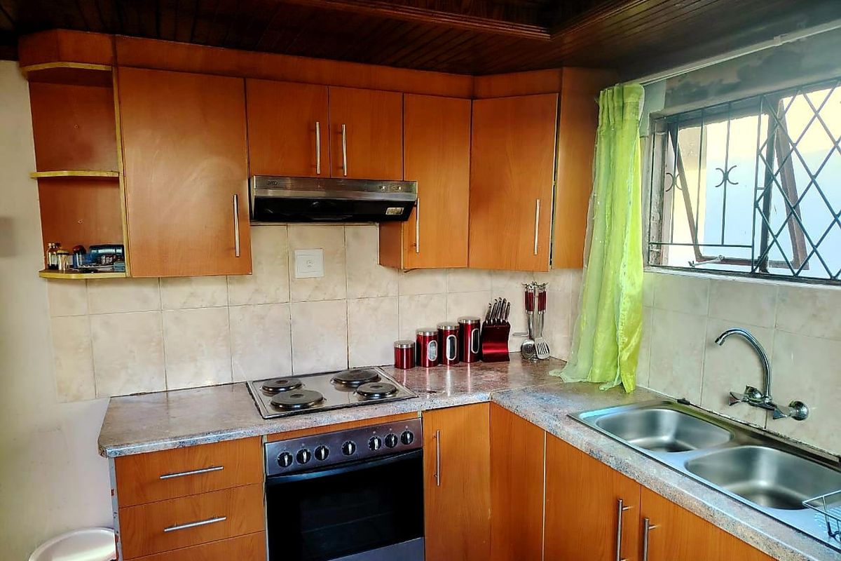 A functional kitchen featuring wooden cabinetry, laminate countertops, a built-in oven with hob, and a tiled backsplash with a timber ceiling.