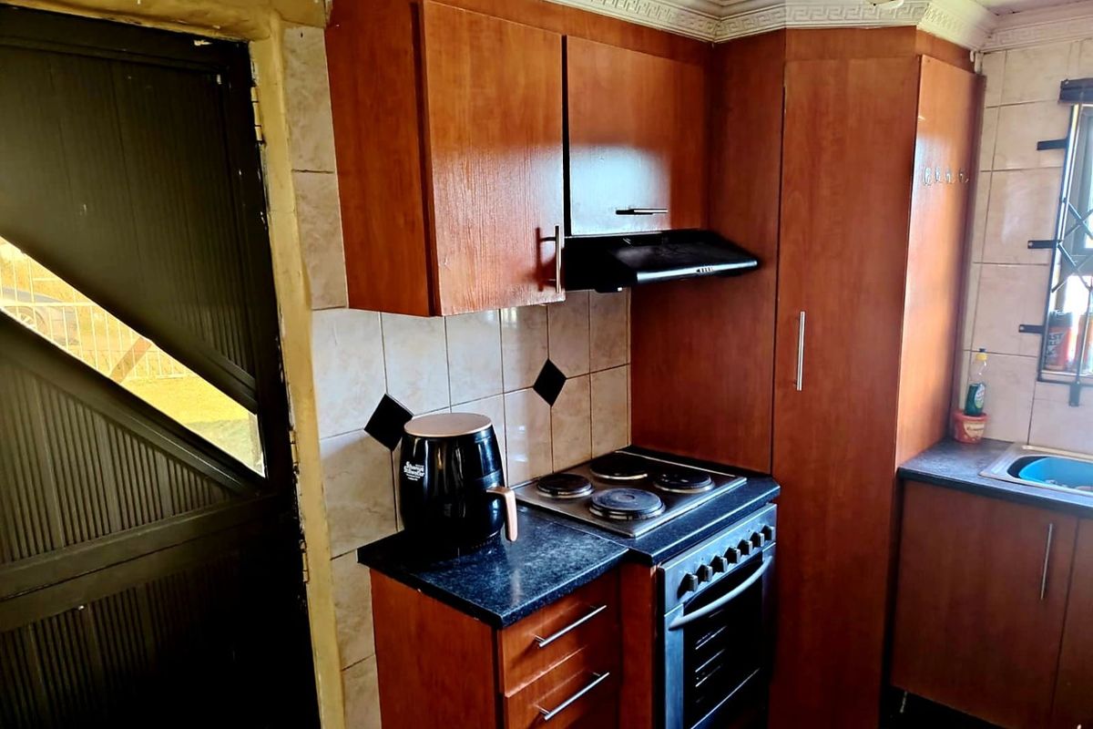 A compact kitchen featuring dated wooden cabinetry, an integrated electric stove with oven, extractor fan, and tiled backsplash.