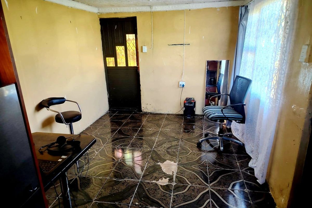 A living area featuring dark patterned floor tiles and a security door, currently requiring cosmetic updates and wall repairs.