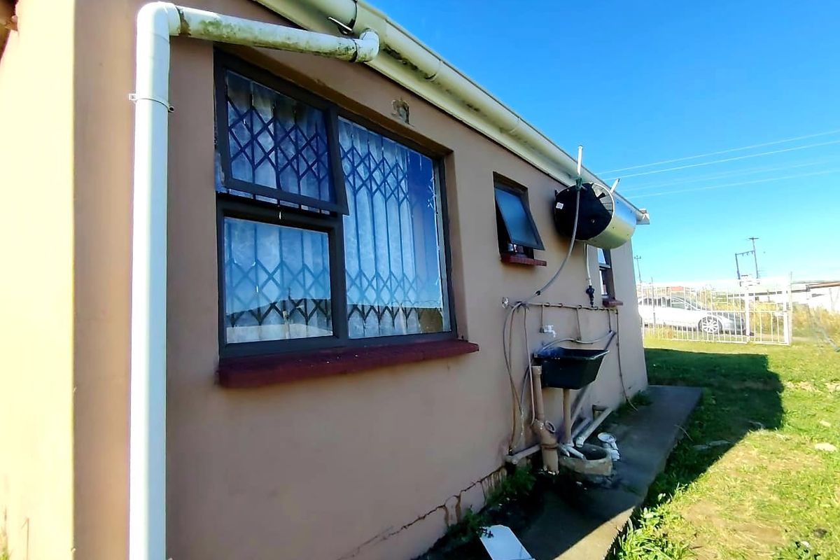 Rear exterior view of the property featuring a solar water heater, security bars on windows, and an external utility sink area.
